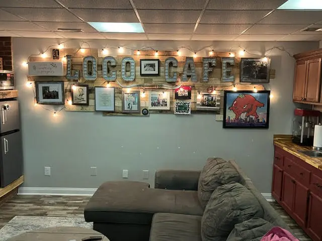 The same basement after: plank flooring, a sectional, a gallery wall of framed photographs, string lights, and marquee letters spelling LOCO CAFE.