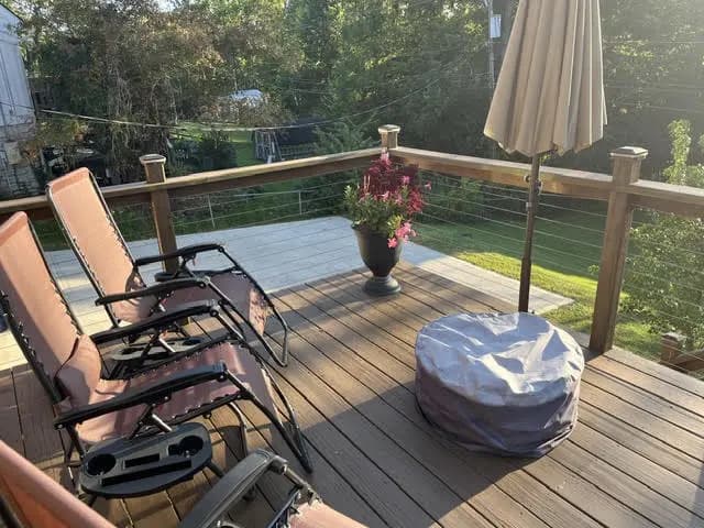 The same deck after: refinished dark boards, black posts with horizontal cable railing, and lounge chairs.