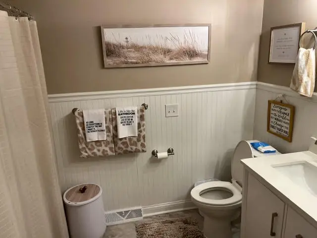 The same bathroom after: white beadboard to chair-rail height, framed artwork, and a white vanity.